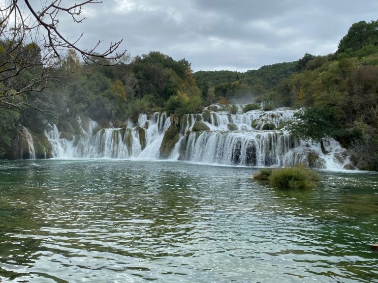 Skradinski Buk Waterfall A cascading waterfall surrounded by lush greenery and a calm blue river.
