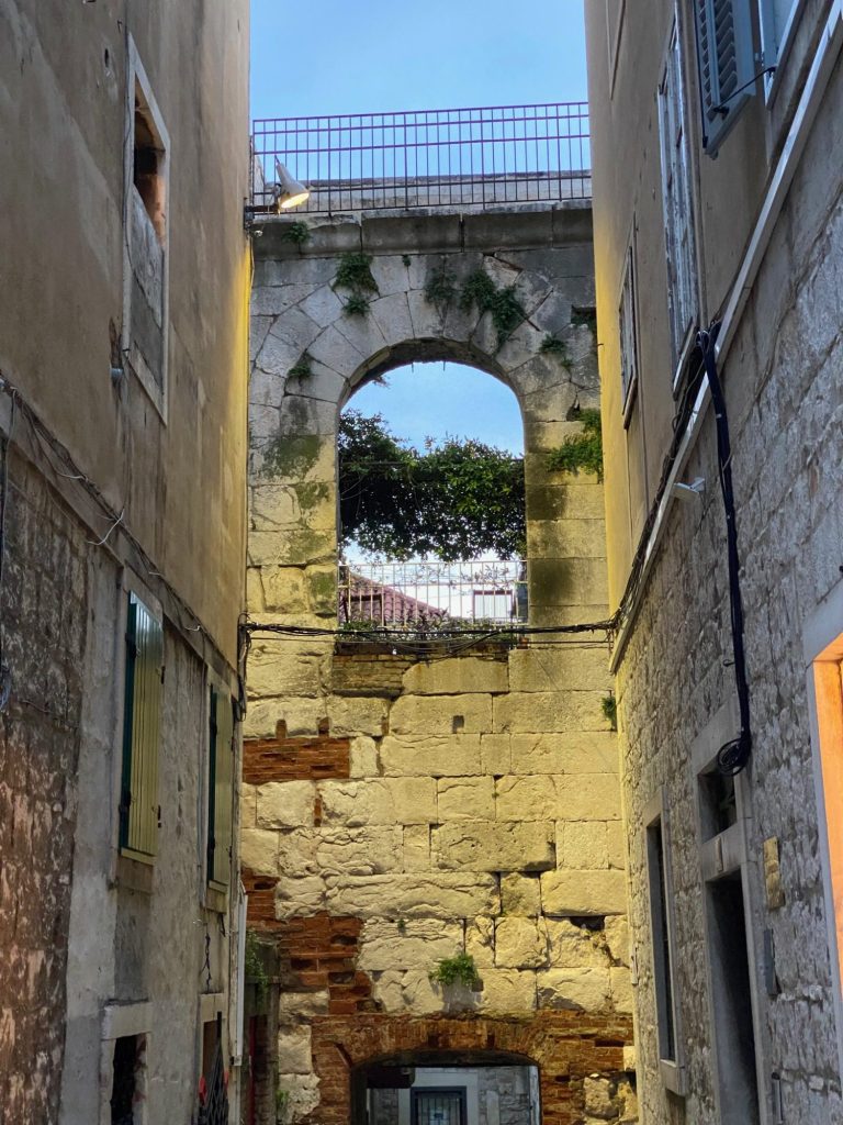 Street of the Old Town Narrow alleyway with ancient stone walls and an archway revealing greenery above.