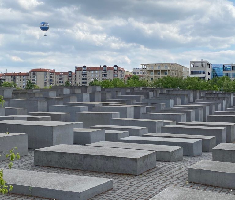 The Holocaust Memorial Memorial with numerous grey concrete blocks under a cloudy sky in an urban setting.