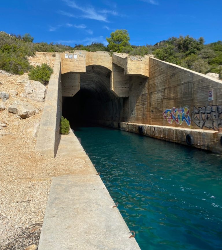 Yugoslavian Ship Hideout Concrete tunnel entrance leading to a turquoise waterway, surrounded by rocky terrain.