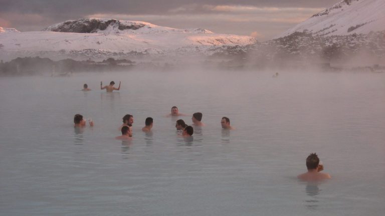 People enjoying a thermal bath with misty surroundings and snowy mountains in the background.