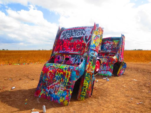Colourfully painted trucks displayed in a barren landscape with blue skies and clouds.