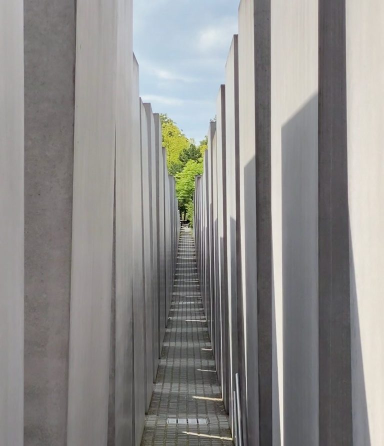 The Holocaust Memorial Narrow pathway between tall grey concrete slabs under a blue sky.