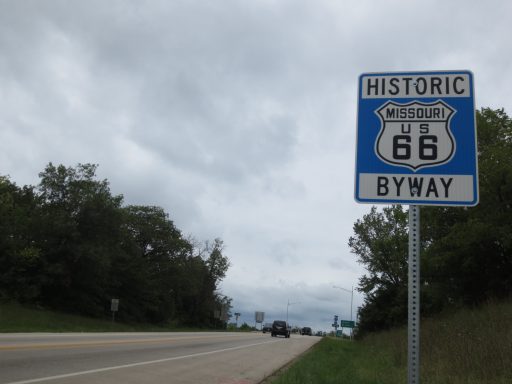 Sign for Historic Route 66 Byway alongside a road, with cloudy skies in the background.