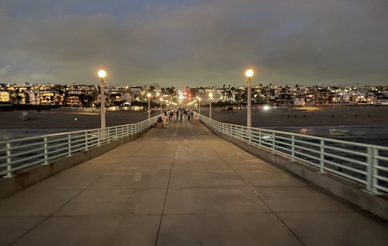 Night view of a pier with streetlights and a city skyline in the background.