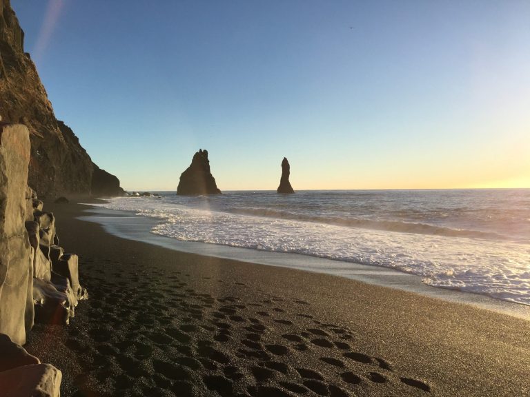 Rocky beach at sunset with two prominent sea stacks and gentle waves.
