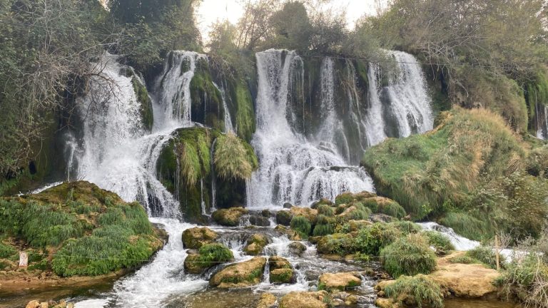 Kravice Waterfalls A cascading waterfall surrounded by lush greenery and rocky terrain.