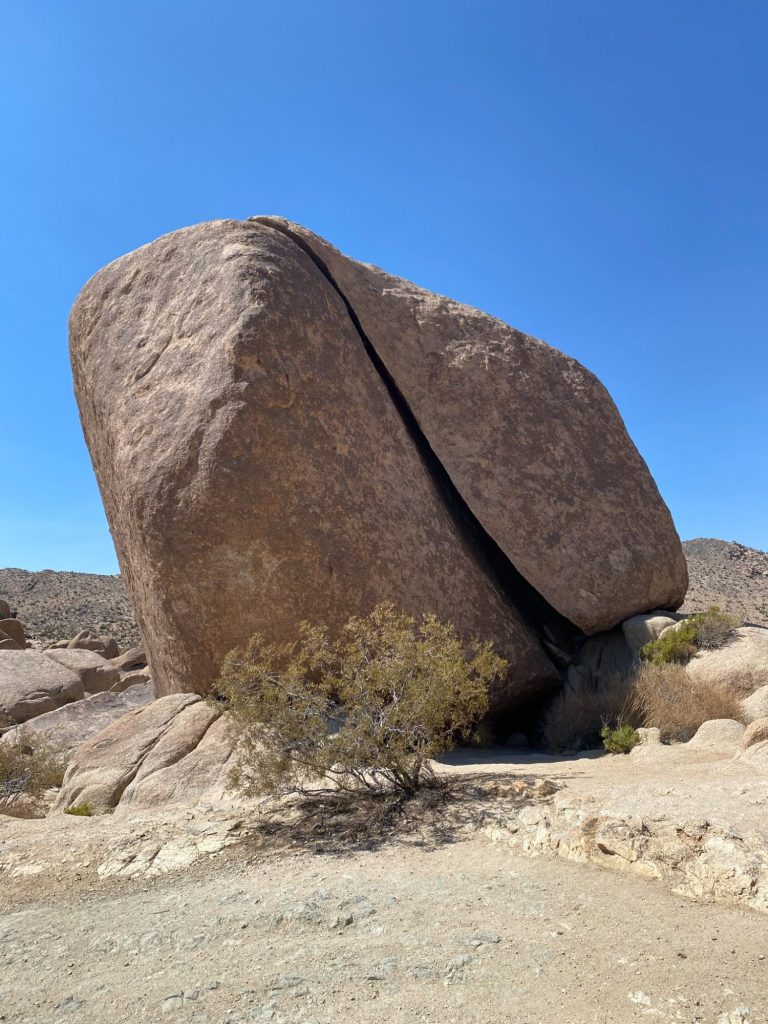 Large, upright boulder with a prominent crack, surrounded by desert landscape.