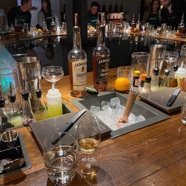 A bar scene with various bottles, mixers, and glasses on a polished wooden counter.