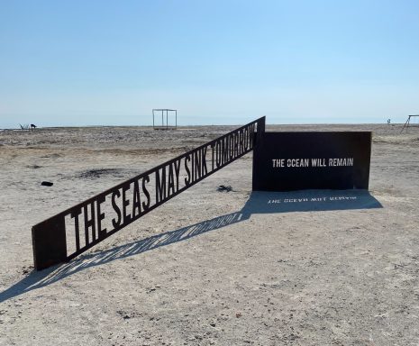 Signage for "The Seas Marvellous" installation on a sandy landscape.