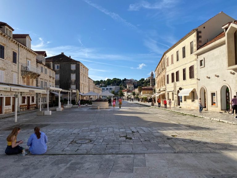 Hvar Town Quiet street scene with stone buildings and people walking in a sunny plaza.