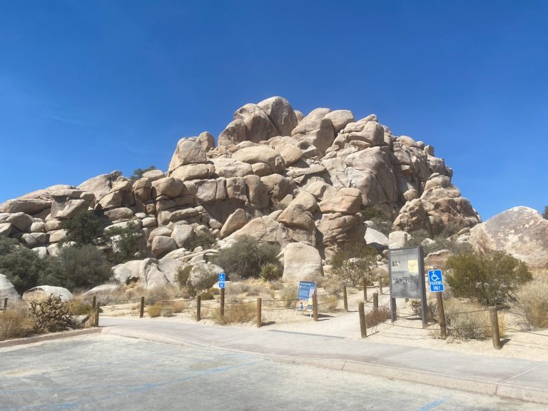 Rocky formation against a clear blue sky, surrounded by dry vegetation and a pathway.