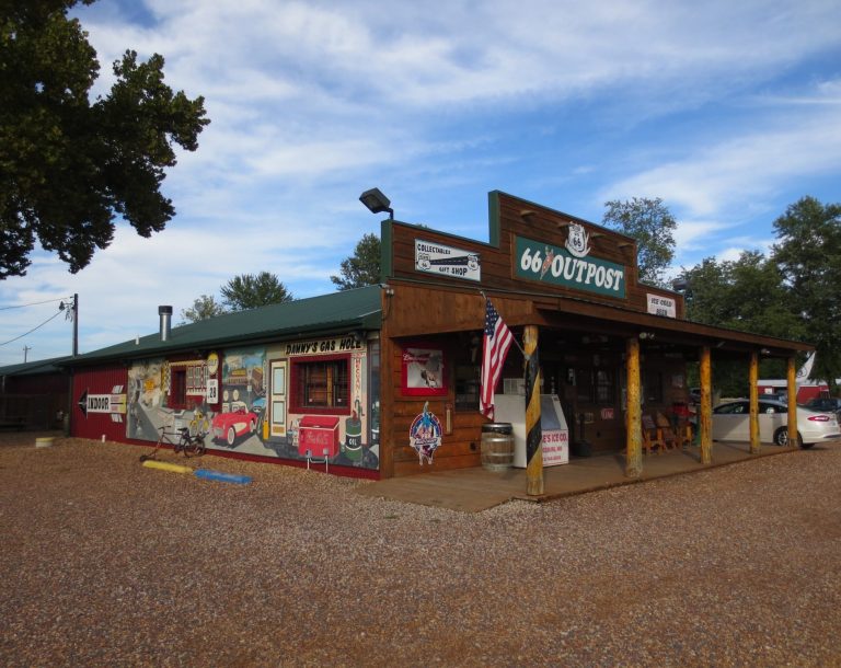 A rustic shop with a wooden facade, colourful murals, and an American flag outside.