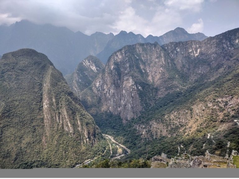 Panoramic view of rugged mountains and lush valleys under a cloudy sky.