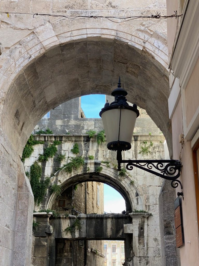 Street of the Old Town Historic archway with a lamp and glimpses of blue sky above.