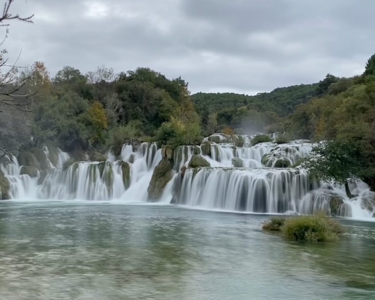 A serene waterfall cascading over rocks into a tranquil pool surrounded by greenery.