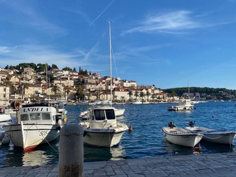 Hvar Harbour Marina with boats on calm water, against a backdrop of a coastal town and blue sky.