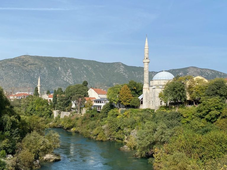 Koski Mehmed Pasha Mosque Scenic view of a river with buildings and a mosque against a mountainous backdrop.