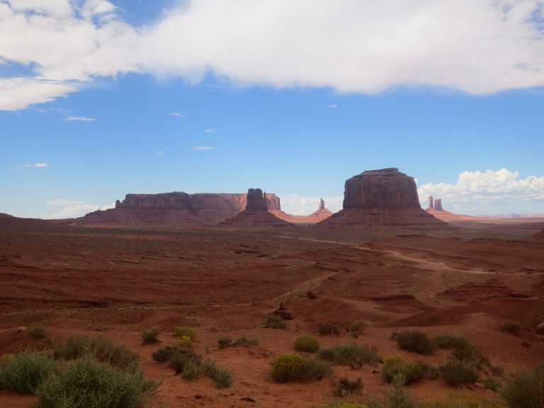 Desert landscape with red rock formations and a blue sky.