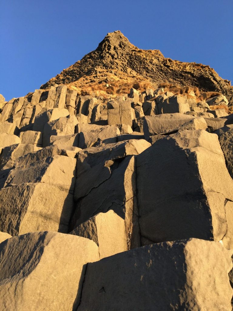 Tall rocky peak under a clear blue sky, with textured stone formations in the foreground.