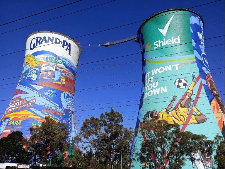 Two large cooling towers adorned with vibrant murals, one featuring "Grandpa" and sports themes.