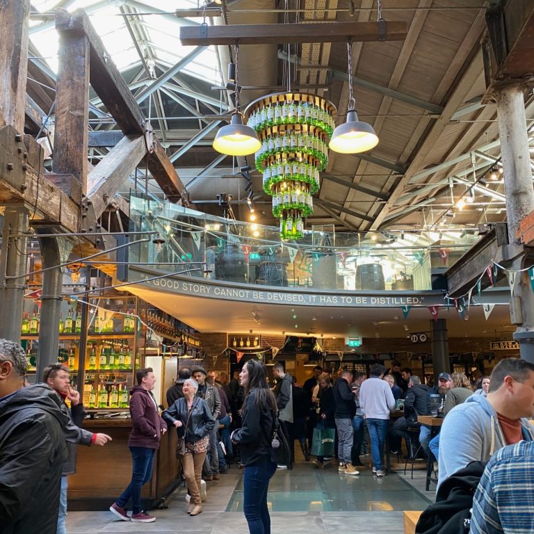Lively market hall with people, decorative lighting, and shelves of colourful goods.