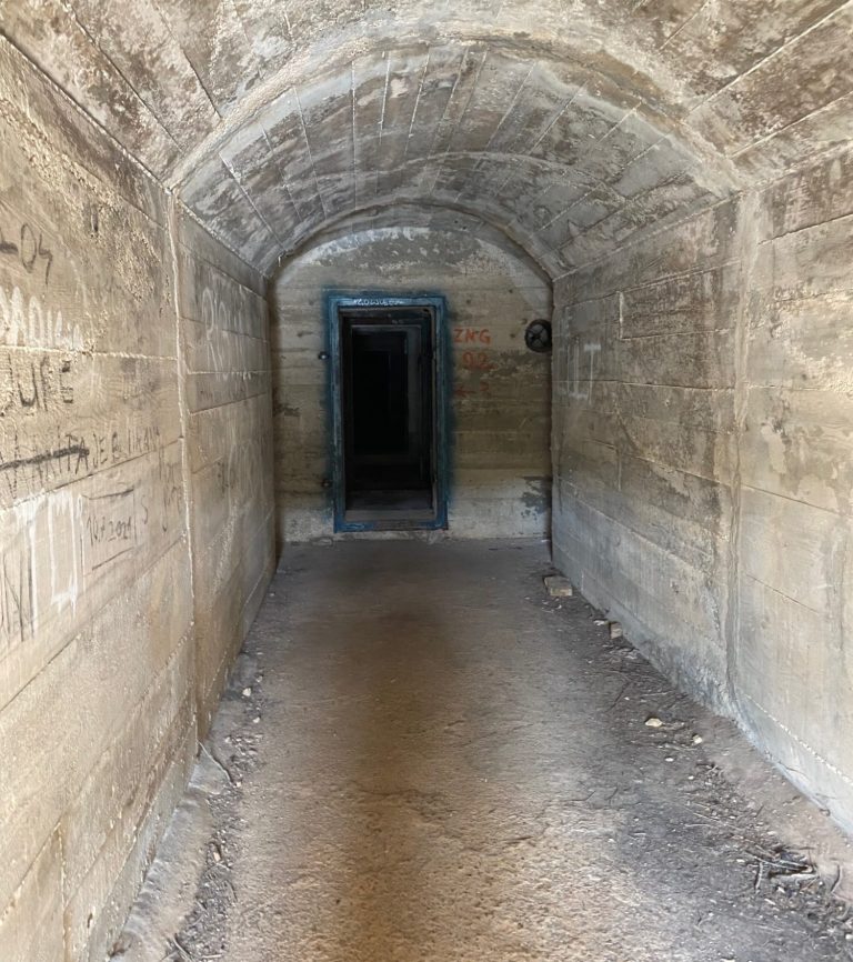 Yugoslavian Ship Hideout Dark, narrow corridor with stone walls and an open doorway at the far end.